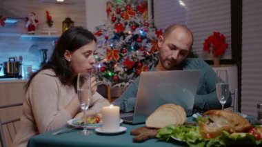 Dizüstü bilgisayara bakan ve Noel yemeğinin tadını çıkaran neşeli çift.