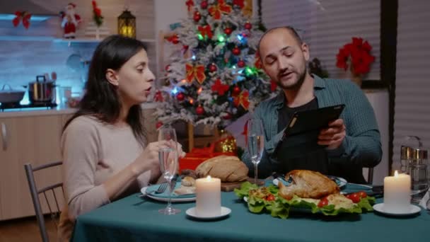 Uroczysta para patrząca na tablet podczas świątecznej kolacji — Wideo stockowe