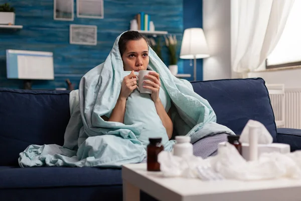 Mujer sintiéndose mal en manta con bebida caliente en casa —  Fotos de Stock