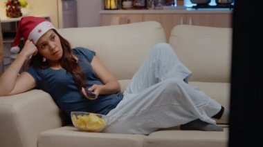 Yorgun bir kadın kanal değiştirip televizyon izliyor.