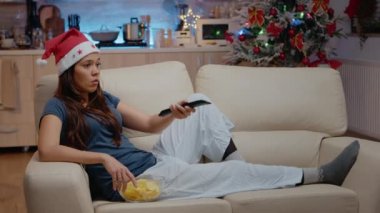 Noel Baba şapkalı kadın televizyon kumandası kullanarak kanal değiştiriyor.