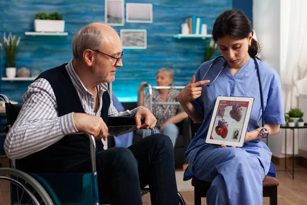 Trabajador de enfermería social explicando la radiografía del cardiograma cardíaco al anciano discapacitado jubilado — Foto de Stock