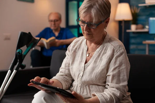 Oudere persoon met krukken op zoek naar moderne tablet — Stockfoto