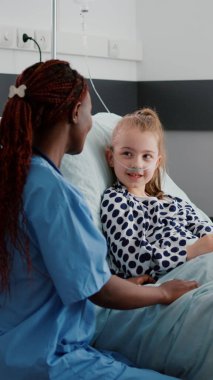 Afrikalı Amerikalı pratisyen hemşire küçük bir hastayla hastalık tedavisini tartışıyor.