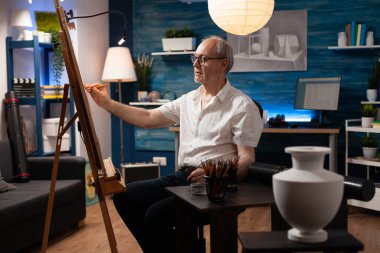 Tablo üzerine kalem çizerek vazo üzerinde çalışan yaşlı bir sanatçı.