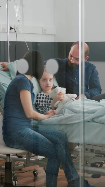 忧心忡忡的父母与生病的女儿坐在一起，等待体检期间的疾病专门知识 — 图库照片