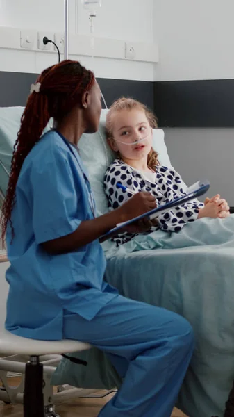 Африканский американский педиатр медсестра обсуждает симптомы болезни с больным маленьким ребенком — стоковое фото