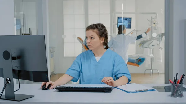 Enfermera de odontología sentada en el escritorio escribiendo en el teclado del ordenador — Foto de Stock