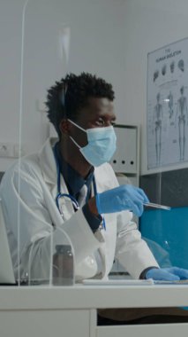 Masadaki engelli kadına yüz maskesi takan doktor.