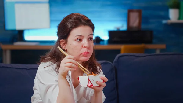 Крупный план деловой женщины, которая ест азиатскую еду на телевидении — стоковое фото