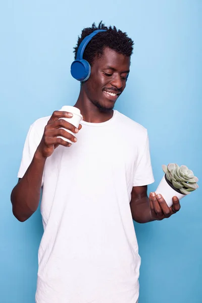 Young adult listening to music and looking at plant in hand — Stock Photo, Image
