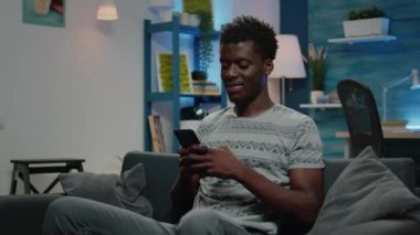 Afro-Amerikan adam gülümsüyor ve akıllı telefon kullanıyor.
