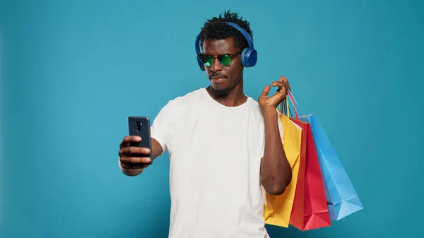 Uomo giocoso scattare foto con borse della spesa su smartphone — Foto Stock