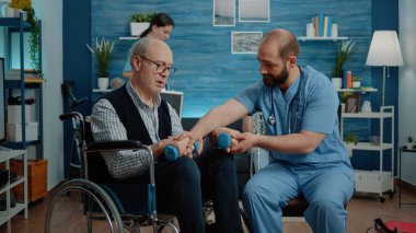 Hemşire engelli adamın halterlerle egzersiz yapmasına yardım ediyor.