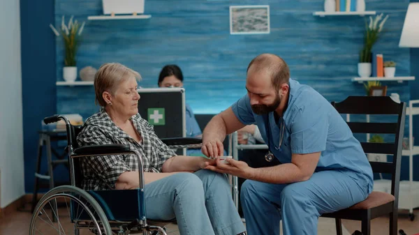 Man nurse putting oximeter on hand of elder disabled woman