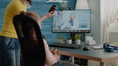 Endişeli ebeveyn videodaki doktora ilaç şişesiyle ilgili sorular soruyor.