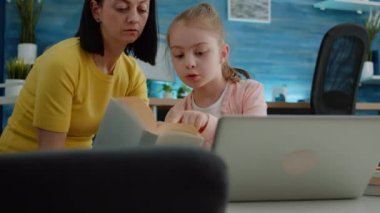 Annemden yardım alarak ev ödevi için dizüstü bilgisayar ve defter kullanan öğrenci.