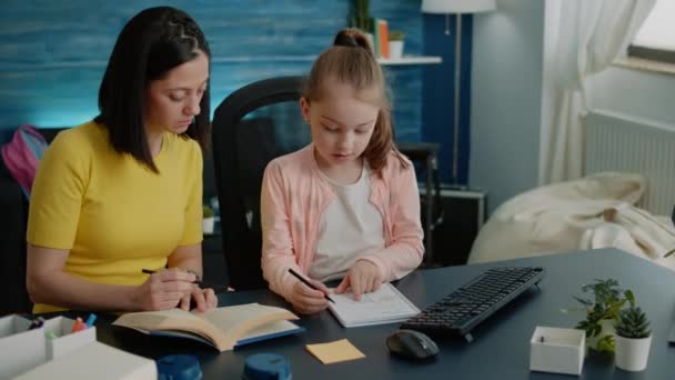 Förälder använder böcker för att hjälpa liten flicka med läxor vid skrivbordet — Stockvideo