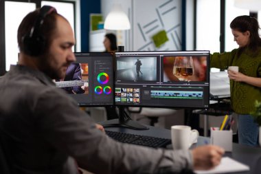 Kulaklıklı video yapımcısı iki ekranlı görüntü ve sesle çalışıyor