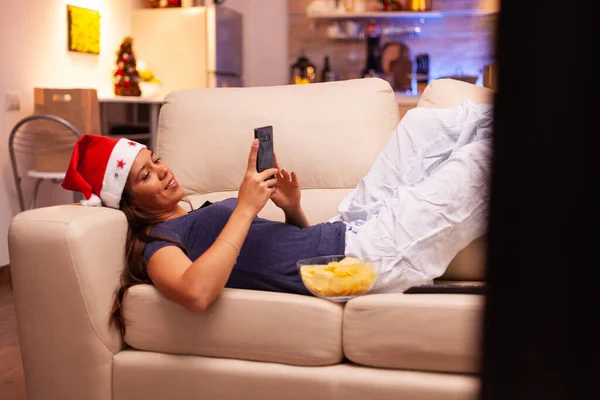 Дівчина обміну повідомленнями з другом за допомогою смартфона відпочиває на дивані — стокове фото