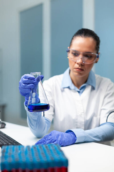 Scientist woman doctor analyzing glassware with blue solution developing healthcare treatment