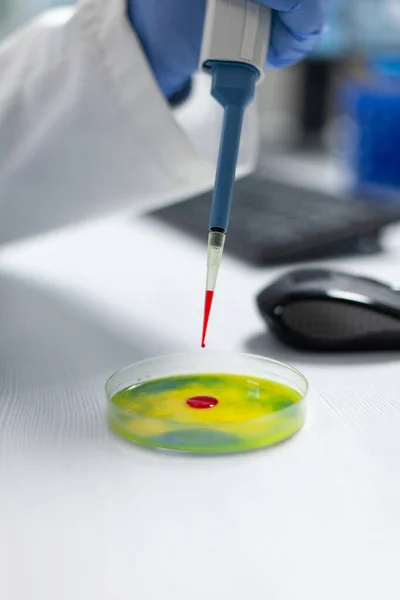 Крупный план биолога-исследователя руки человека, сбрасывающего красную жидкость в чашку Петри — стоковое фото