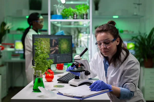 Biokemist läkare kvinna analysera gmo växter prov med hjälp av medicinskt mikroskop — Stockfoto