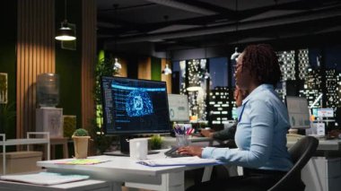 Siyahi kadın uzman KPI raporlarını bilgisayarda yapay zeka araçlarıyla inceleyerek yapay zeka ağlarıyla makine öğrenimi için çalışıyor. Yenilik ve optimizasyon vurgulanıyor. Kamera A.