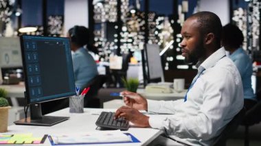 Erkek siyahi çalışan yapay zeka sanal asistanı kullanımına odaklanıyor. Monitörde. Fütürist teknoloji ve makine öğrenme ile problem çözme görevlerini çözüyor. İletişim ve bilişim desteği. Kamera B.