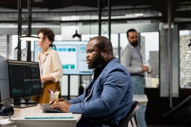 Siyah yönetici, çok uluslu bir şirket ofisindeki iş performansını tahmin etmek için dijital teknolojiyi kullanır, yönetim verimliliğini optimize etmek için veri içgörülerini koz olarak kullanan strateji raporları oluşturur..