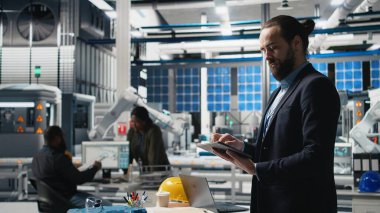 Endüstriyel erkek giysi uzmanı güneş enerjisi ekipmanlarını denetliyor, kalite kontrol ve üretim hattında verimlilik gösteriyor. Güneş panelleri üretiminde çalışıyorum. Kamera A.