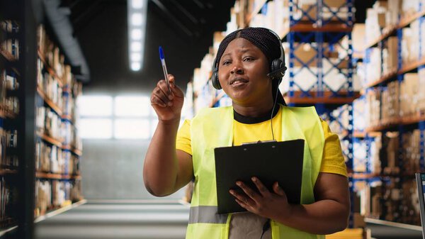 Black customer service worker speaks with clients about cargo issues, helping with the parcel information from the industrial warehouse. Woman resolves order mix up on headset. Camera B.