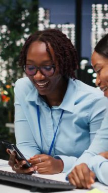 Dikey Video İki iş kadını hedeflere ulaşmak için birlikte çalışıyor, proje teslim tarihlerini karşılamak için saatler sonra takım çalışması yapıyor. İş verimliliği için KPI numaralarını inceleyen personel. Kamera B.