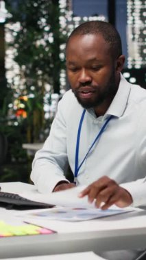 Dikey Video Siyah genç çalışanı, gece yeni bir rapor için finansal verileri düzeltiyor, strateji odasındaki arşivlenmiş dosyaları inceliyor. Veriler değerlendiriliyor, araştırılıyor ve gündem düzenleniyor. Kamera B.