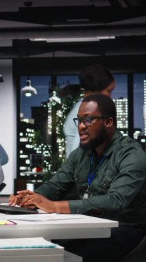 Dikey Video Afrikalı Amerikalı Danışmanı, geceleri karanlık bir ofiste karmaşık bir soruna odaklanarak, masaüstü seçenekleri tasarlıyor ve öngörüyor. Dikkatli sonuç çıkararak mantıklı bir çözüm arıyorum.