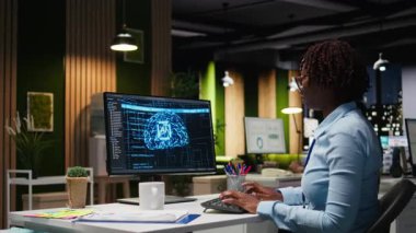 Uzman analist bilgisayardaki yapay zeka araçlarıyla KPI raporlarını inceleyerek, makine öğrenimi için yapay zeka ağlarıyla çalışıyor. Yenilik ve optimizasyon vurgulanıyor. Kamera A.