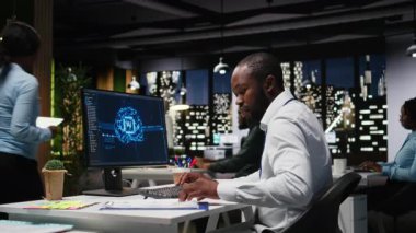 Bilgisayarda yapay zeka araçlarıyla KPI metrik verilerini kontrol eden Afrikalı Amerikalı işçiler, makine öğrenimi için yapay zeka ağlarıyla çalışıyorlar. Yeniliğin altını çiziyorum. Kamera A.