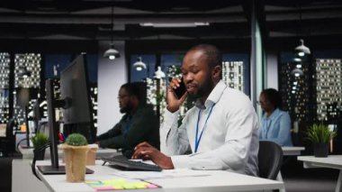 Erkek çalışan, iş arkadaşıyla uzaktan görüşme için telefona cevap veriyor. Telefon hattındaki ortak bir sohbet sırasında gülümsüyor. Gece geç saatlerde yeni bir projeyi koordine etmek için uygunluk. Kamera A.