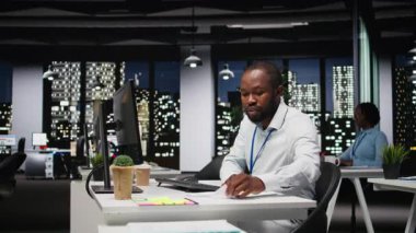 Siyah genç çalışan, gece yeni bir rapor için finansal verileri düzeltiyor, strateji odasındaki arşivlenmiş dosyaları inceliyor. Veriler değerlendiriliyor, araştırılıyor ve gündem düzenleniyor. Kamera A.