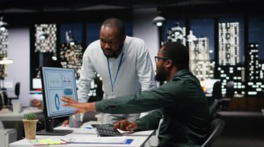 Afrika kökenli Amerikalı işçiler geceleri görev çözmede birbirlerine danışırlar, aylık raporları tamamlarlar ve verimlilik için KPI verilerini incelerler. Başarı için işbirliği. Kamera B.