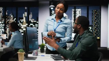 Afrika kökenli Amerikalı işçiler geceleri görev çözmede birbirlerine danışırlar, aylık raporları tamamlarlar ve verimlilik için KPI verilerini incelerler. Başarı için işbirliği. Kamera B.