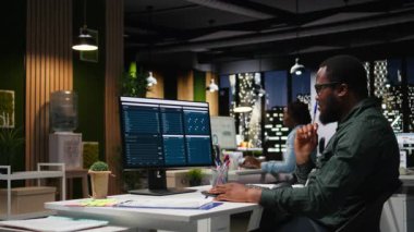 KPI ölçümlerini monitörde ve masaüstünde inceleyen ofis çalışanı, hedeflere ve başarıya ulaşmak için bir vizyon ve iş stratejisi oluşturmaktadır. Mesai sonrası profesyonel zihniyet. Kamera A.