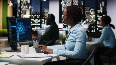 KPI ölçümlerini PC monitöründe yapay zeka ile inceleyen Afrikalı Amerikalı bir kadın yapay zeka ile derin öğrenim için yapay zeka ağları üzerinde çalışıyor. Yenilik ve optimizasyon vurgulanıyor. Kamera B.