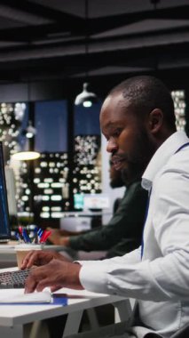 Bilgisayarda yapay zeka araçlarıyla KPI metrik verilerini kontrol eden dikey video Afrikalı Amerikalı işçiler, makine öğrenimi için yapay zeka ağları ile çalışıyorlar. Yeniliğin altını çiziyorum. Kamera A.