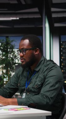 Dikey Video Afrikalı Amerikalı Danışman gecenin geç saatlerinde bir not defterinden bilgi alıyor ve işletme yönetiminin finans raporlarından özetler hazırlıyor. Not alma hedef ayarlarını destekler