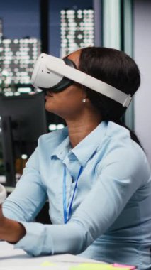 Dikey Afrikalı Amerikalı kadın yapay zeka aygıtını karanlık ofiste kullanıyordu. Projeksiyonların doğruluğunu kontrol etmek ve analiz etmek için şirketin çalışma alanında VR gözlükleriyle fazla mesai yapıyordu.