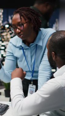 Dikey Video İki siyahi işçileri masadaki sanal bir asistanla etkileşime geçtiler, yapay zeka ve akıllı otomasyon ile çevrimiçi iletişimi geliştirdiler. Veri güdümlü yapay zeka çözümleri. Kamera.