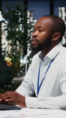 Dikey Video Afrikalı Amerikalı çalışanlar aylık raporlar için birbirlerine danışıyorlar, gece geç saatlerde iş verimliliği için KPI veri içgörülerini gözden geçiriyorlar. Çalışanlar arasındaki işbirliği