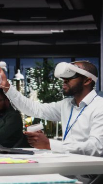 Dikey Video Siyah işadamı VR kulaklık ve cihazlar kullanarak bir proje planı hazırlıyor, tahminlerde bulunuyor ve risk değerlendirme sonuçlarını belgeliyor. Sanal gerçeklikle görevleri çöz