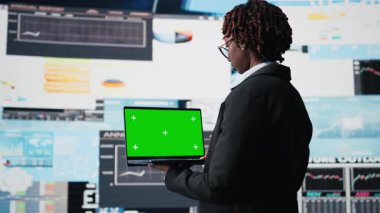 Performans gösterge tablosu ölçülerini incelemek için yeşil ekran bilgisayarı kullanan bir iş uzmanı. Renkli anahtar not defteri, kamera A kullanarak yıllık rapor verilerini değerlendiren yönetim yöneticisi